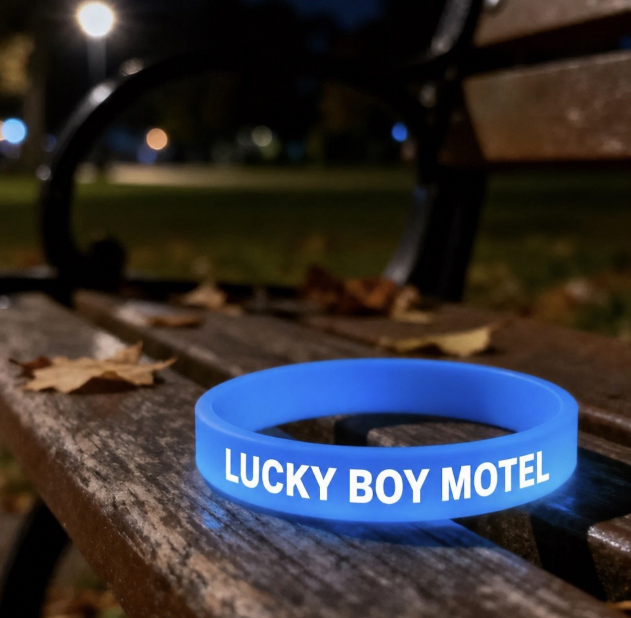 Blue glowing Lucky Boy Motel wristband on a bench at night.